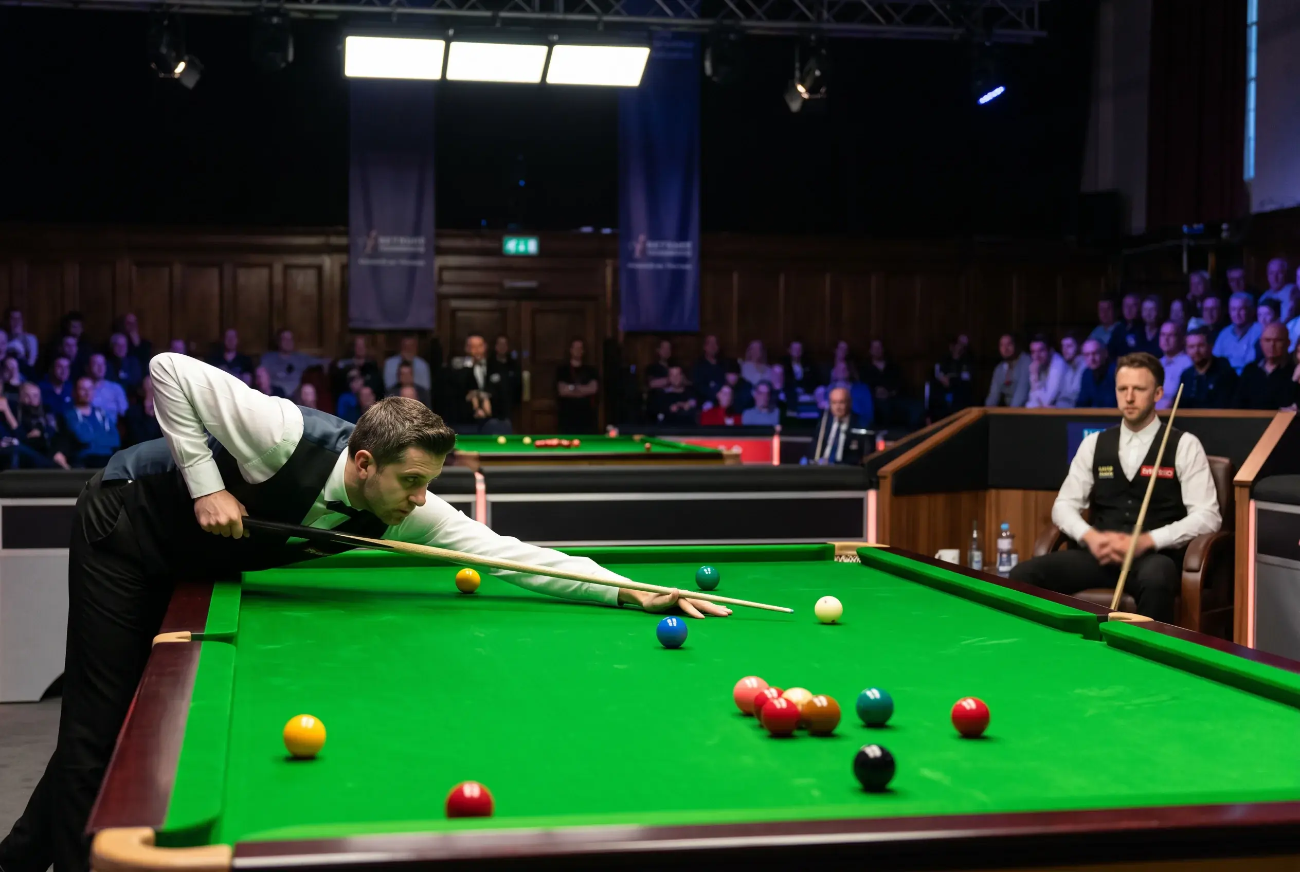 Zwei Snookerspieler am Turniertisch während eines Matches unter Bühnenbeleuchtung