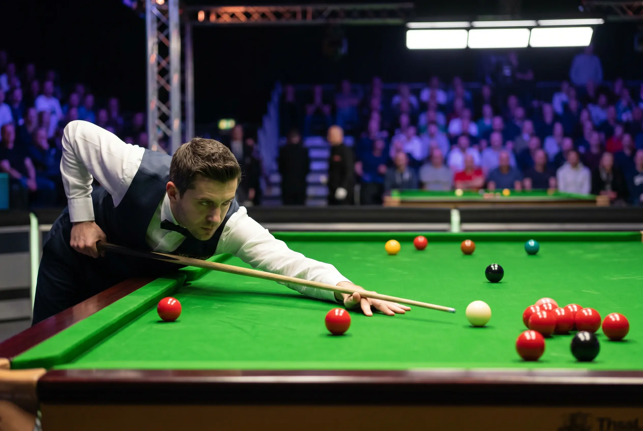 Snookerspieler am Tisch beim langen Stoß mit ausgestrecktem Queue und roten Bällen