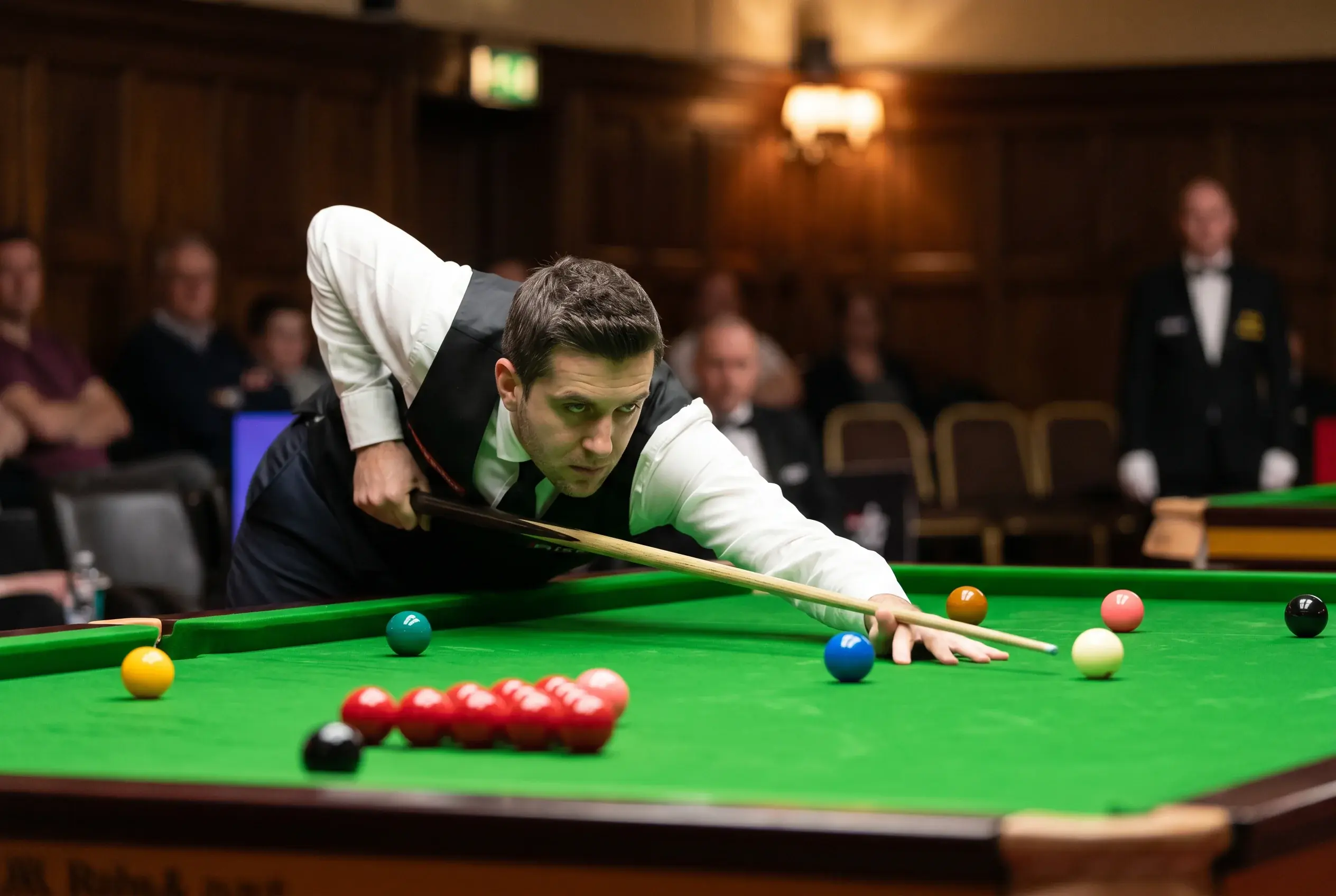 Snooker-Profispieler beim Stoß am grünen Snookertisch mit roten und farbigen Bällen